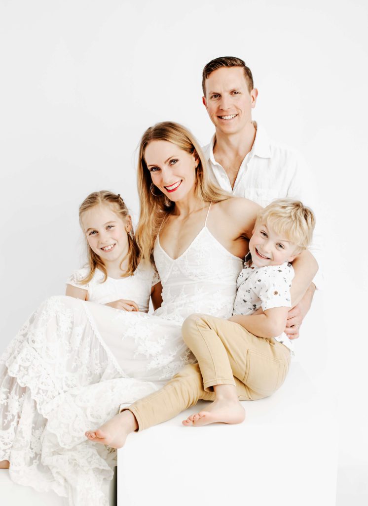 Family portrait on a simple white backdrop, by lauren Vanier Photography. There is a mum, dad, son and daughter, all smiling for the camera